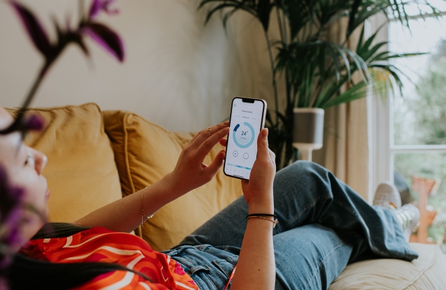 A woman reclines on a sofa, checking some figures on a mobile phone 