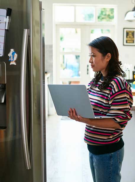 Woman with laptop near open fridge