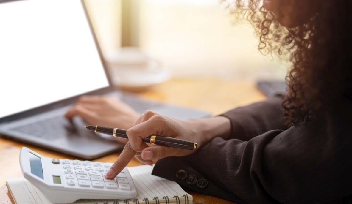 A young woman uses a calculator whilst working on a laptop computer