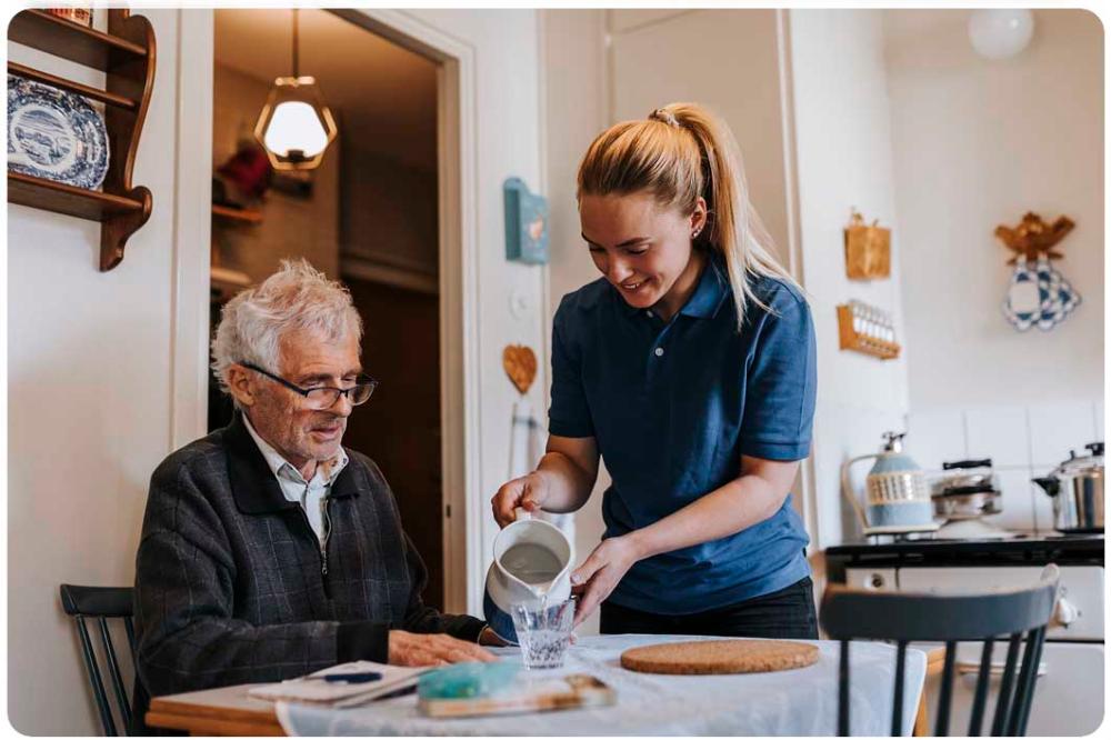 Elderly man being poured a drink by a carer